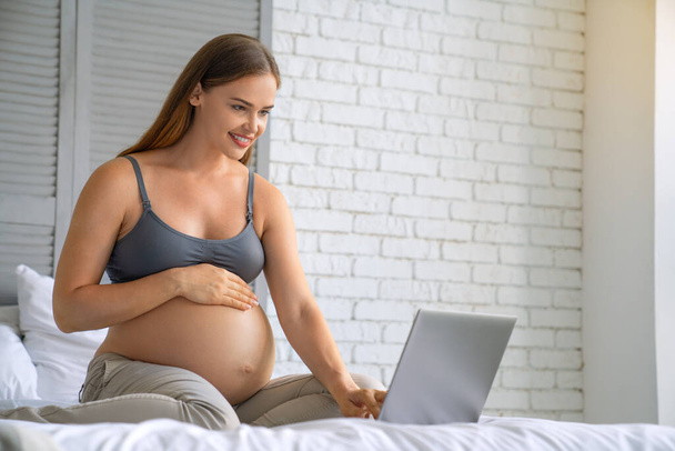 Young pregnant woman relaxing on sofa with laptop on home interior background - Fotoğraf, Görsel