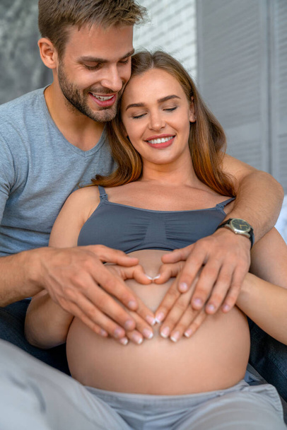 Vertical shot of young couple making a heart shape on the pregnant belly with their hands - Foto, Imagem