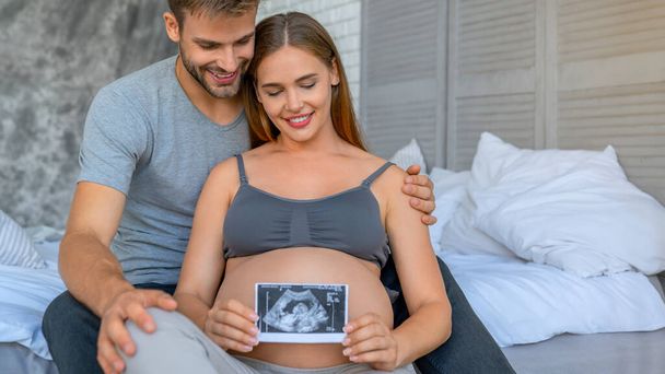 Beautiful pregnant woman and her handsome husband looking a baby ultrasound scan photos - Fotografie, Obrázek