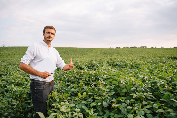 Portrait of young farmer standing in soybean field. - Фото, зображення