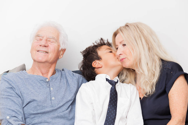 Junge küsst ihre Großmutter. Senioren mit Enkelkind auf Sofa. Konzept Familie, Teilen und Freude - Foto, Bild