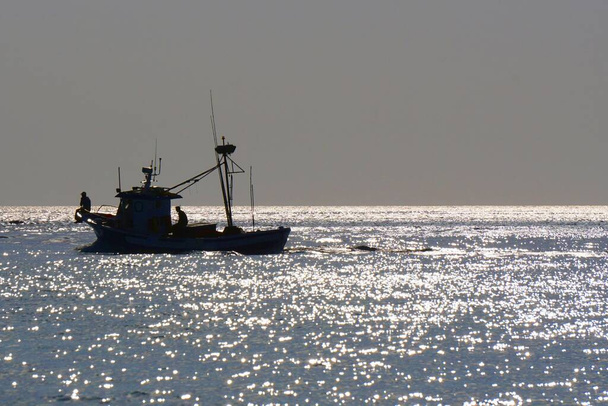  Tag im Atlantik. Silhouette eines Fischerschoners und gleißendes Licht auf den Wellen. Viel Sonne                               - Foto, Bild