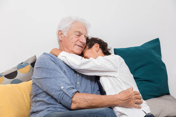 Glücklicher Junge kuschelt seinen Großvater auf einem Sofa. Konzept von Zärtlichkeit, Familie und Freude - Foto, Bild