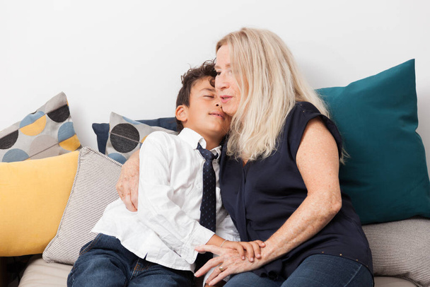 Το χαρούμενο αγόρι αγκαλιάζει τη γιαγιά του σε έναν καναπέ. Έννοια της τρυφερότητας, της οικογένειας και της χαράς - Φωτογραφία, εικόνα