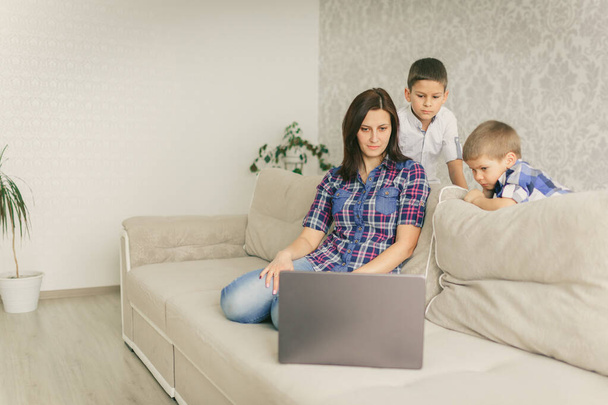 自宅にいて、お母さんと子供たちはノートパソコンでビデオ会議を見ています。在宅勤務社会的距離の概念。隔離だ。閉じ、コピースペース、背景. - 写真・画像