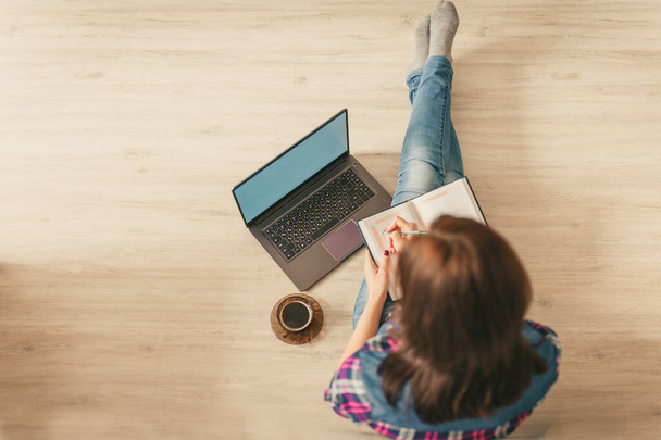 Das Mädchen sitzt zu Hause mit Laptop und Tagebuch auf dem Fußboden. Soziales Distanzkonzept. - Foto, Bild