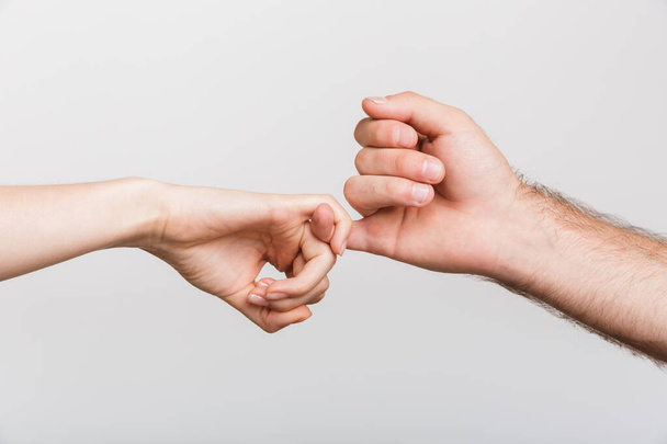 Closeup image of a man's and woman's hands holding little fingers of each other isolated over white wall background. - Foto, immagini