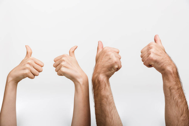 Closeup image of a man's and woman's raised hands isolated over white wall background showing thumbs up gesture. - Photo, image