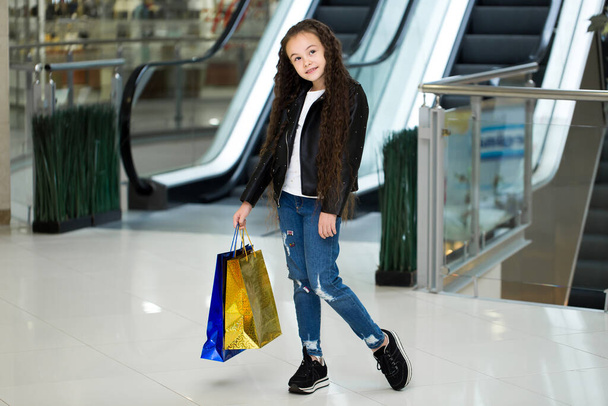 A criança feliz com pacotes a cores na escada rolante, na loja do centro comercial
. - Foto, Imagem