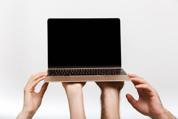 Closeup picture of a man's and woman's hands isolated over white wall background holding laptop computer showing empty display. - Foto, Imagen