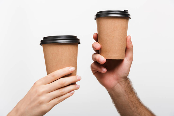 Closeup image of a man's and woman's hands isolated over white wall background holding cups with coffee. - Valokuva, kuva