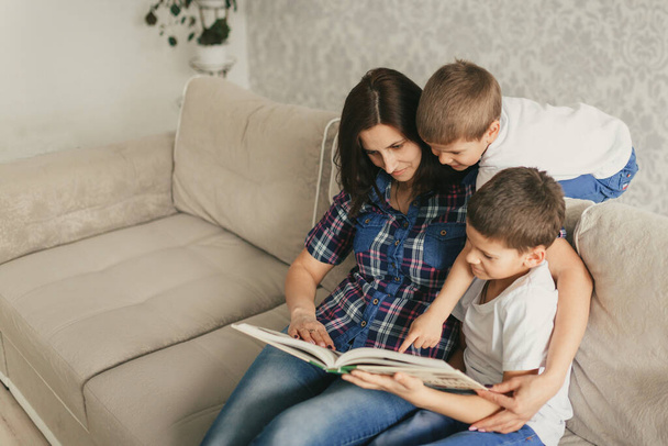 madre con i figli che leggono un libro mentre sono seduti su un divano in soggiorno durante la quarantena. Il concetto di distanza sociale, auto-isolamento e scuola a casa.Focus selettivo
 - Foto, immagini