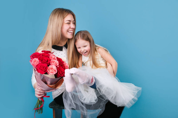 青い背景に花の花束を持つ小さなかわいい娘と母親。母の日のコンセプト - 写真・画像