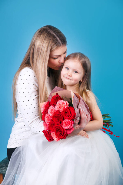 moeder en dochter met bloemen knuffelen op blauwe achtergrond. - Foto, afbeelding