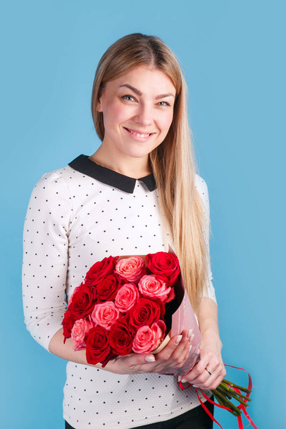 Happy beautiful woman with bouquet of red roses smilling over blue studio background. - Photo, Image