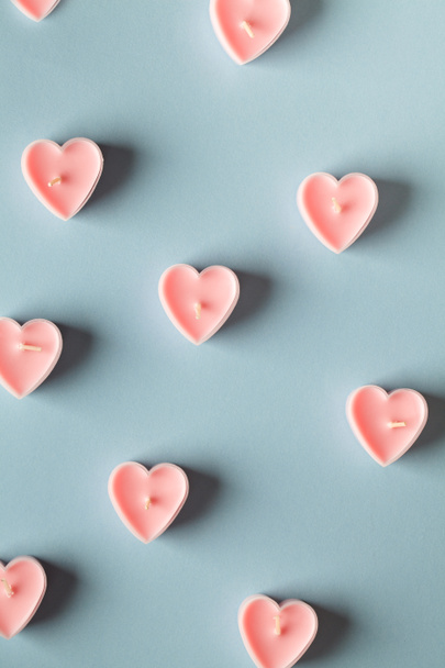 ピンクのハート型のキャンドルが青の背景に。バレンタインデーミニマリストの背景。ピンクハート愛のシンボルグリーティングカードのグラフィックデザイン要素 - 写真・画像