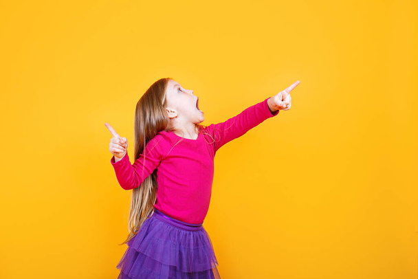 Wow look. Portrait of amazed cute little surprised girl preschooler showing copy space on yellow background - Foto, afbeelding