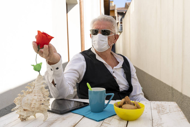 adult man is having breakfast while working on the tablet outdoors during the coronavirus emergency - Photo, image