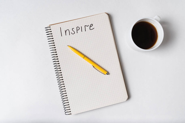 Надпись INSPIRE в блокноте. Блокнот, ручка и кофе на белом фоне
. - Фото, изображение