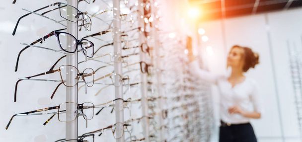 Row of glasses at an opticians. Eyeglasses shop. Stand with glasses in the store of optics. Woman chooses glasses. Presenting spectacles - Foto, Imagem