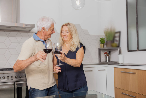 Mutlu son sınıf çifti evde mutfakta konuşurken ve kırmızı şarap içerken rahatlıyor. - Fotoğraf, Görsel