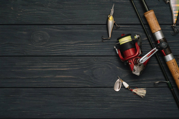 Fishing tackle - fishing spinning, hooks and lures on darken wooden background. Top view. - 写真・画像