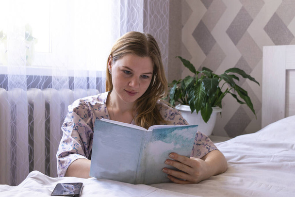 Fiatal nő dolgozik irodai munka távolról otthonról az ágyban. Számítógép, telefon és könyv.Távolsági tanulás online oktatás és a munka. Maradj otthon.. - Fotó, kép