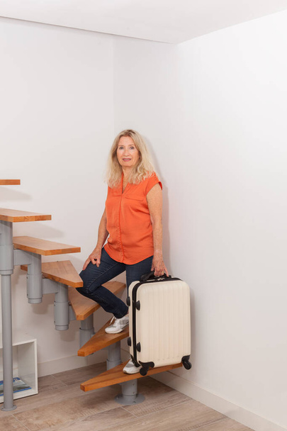 スーツケース付きの階段のブロンドのシニア女性。旅行と休暇のコンセプト - 写真・画像