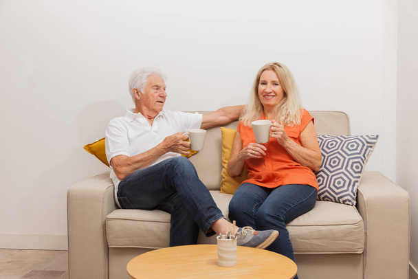 Feliz pareja de ancianos bebiendo un té, sentados en el sofá en la vida
 - Foto, imagen