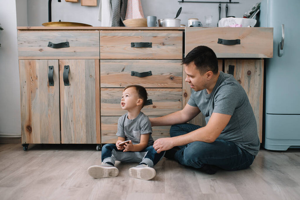 Mladý muž a jeho syn s prostěradlem v kuchyni. Otec s malým synem v kuchyni - Fotografie, Obrázek