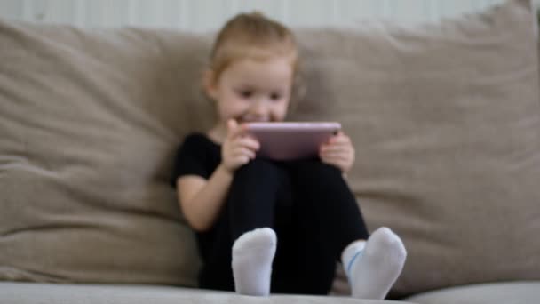 Distance learning, online education for kids. Little girl studying at home in front of the smartphone. Child watching online cartoons, kids computer addiction, parental control. Quarantine at home - Záběry, video