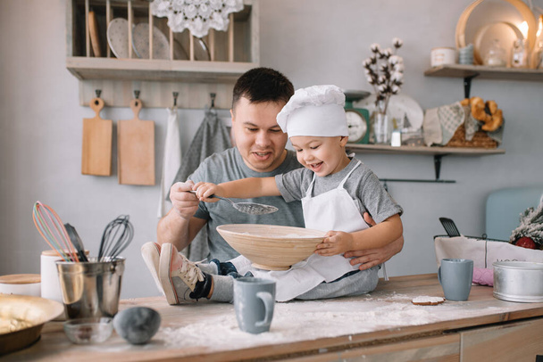 Young man and his son with oven sheet in kitchen. Father with little son on the kitchen - Фото, изображение