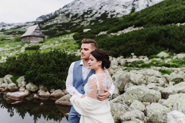 Bela noiva e noivo abraço e beijo nas montanhas perto do lago
. - Foto, Imagem