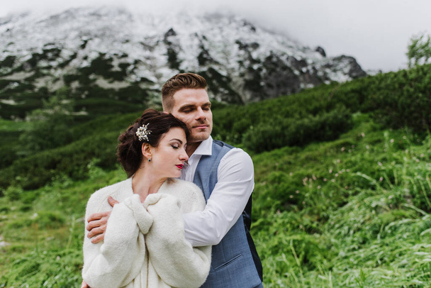 Schöne Braut und Bräutigam umarmen und küssen sich in den Bergen. - Foto, Bild