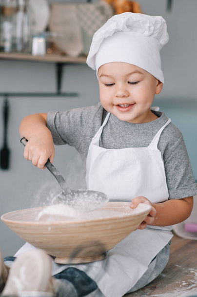 Young boy cute on the kitchen cook chef in white uniform and hat near table. homemade gingerbread. the boy cooked the chocolate cookies - 写真・画像