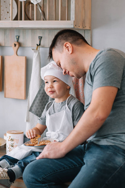 Молодой человек и его сын с духовкой на кухне. Отец с маленьким сыном на кухне
 - Фото, изображение