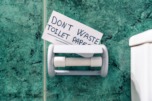 Fertige Toilettenpapierrolle im Badezimmer. Toilettenpapier nicht verschwenden, es ist auf Papier geschrieben. - Foto, Bild