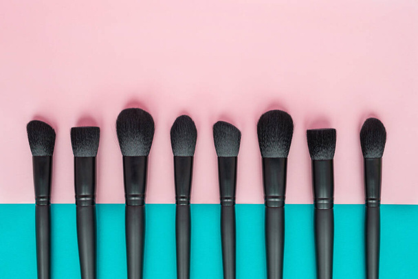 Flat lay of black makeup brushes on a pink and blue background - Foto, Imagem
