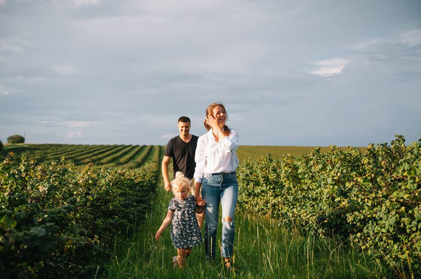 Happy family with little daughter spending time together in sunny field - Foto, afbeelding