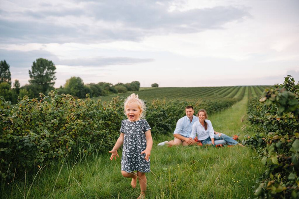 Happy family with little daughter spending time together in sunny field - Fotografie, Obrázek