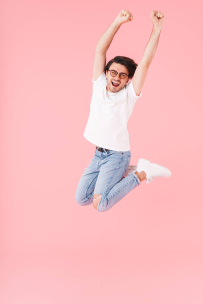 Bild eines gut aussehenden aufgeregten Mannes mit Brille, der mit erhobenen Armen auf rosa Hintergrund springt - Foto, Bild