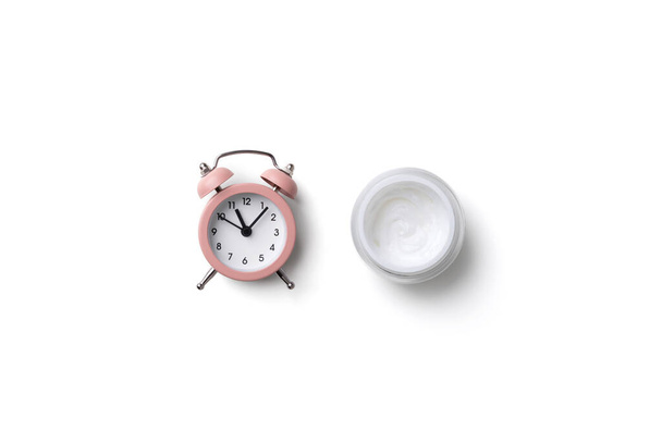 Wekker klok en cosmetica crème op witte achtergrond - Foto, afbeelding