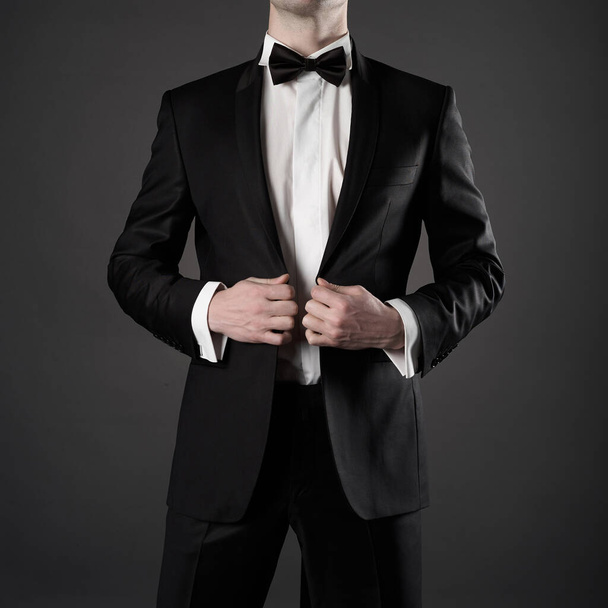 Photo of stylish man in elegant black suit with tie. Fashionable young model pose in photography studio. Luxury evening smoking with white shirt. - Zdjęcie, obraz