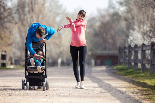 Tiro de jovem casal esportivo com seu filho pequeno se alongando enquanto caminhava e aproveitando o tempo juntos ao ar livre
. - Foto, Imagem