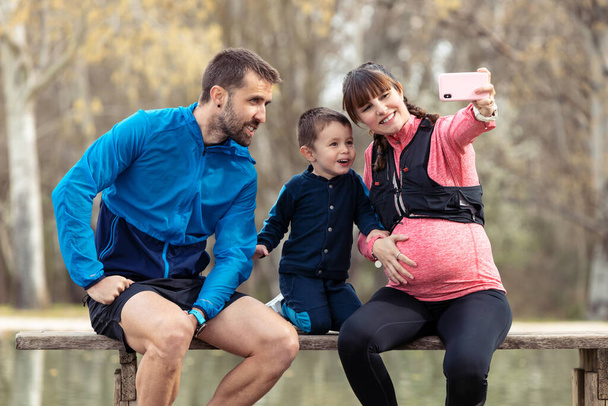 Shot of happy young family taking a selfie with the smartphone while enjoying the time together outdoor. - Φωτογραφία, εικόνα