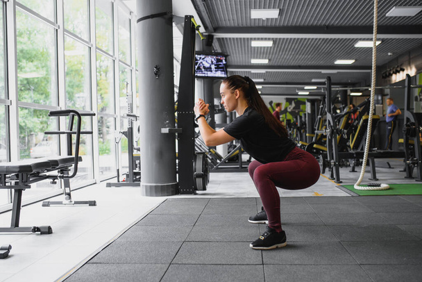 Side view portrait of a young woman doing squats at fitness gym - Фото, зображення