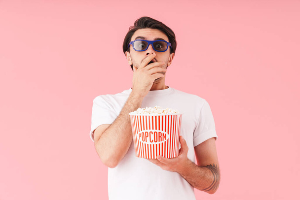 Image of shocked scared man wearing 3d glasses eating popcorn while watching movie isolated over pink background - Fotografie, Obrázek