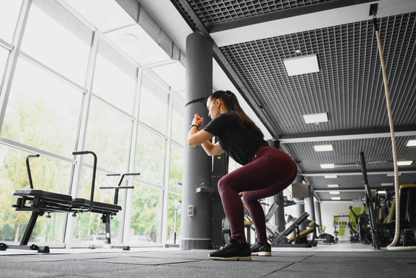 Side view portrait of a young woman doing squats at fitness gym - Fotó, kép