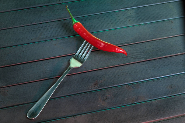 Red hot chili pepper on a fork. Pepper on the dark boards of the table. Bright red and dark turquoise colors. - Foto, immagini