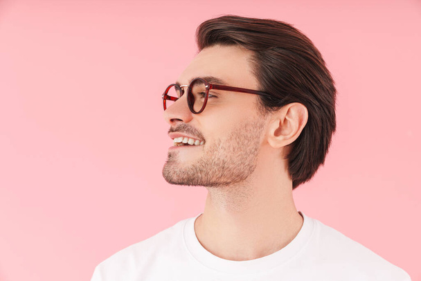 Image in profile of funny caucasian man wearing eyeglasses smiling and looking forward isolated over pink background - Foto, Bild